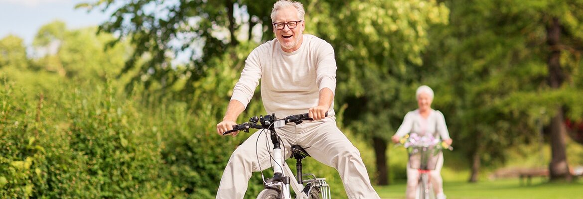 Veselý starší pán jede na kole a radostí zvedá nohy do vzduchu.